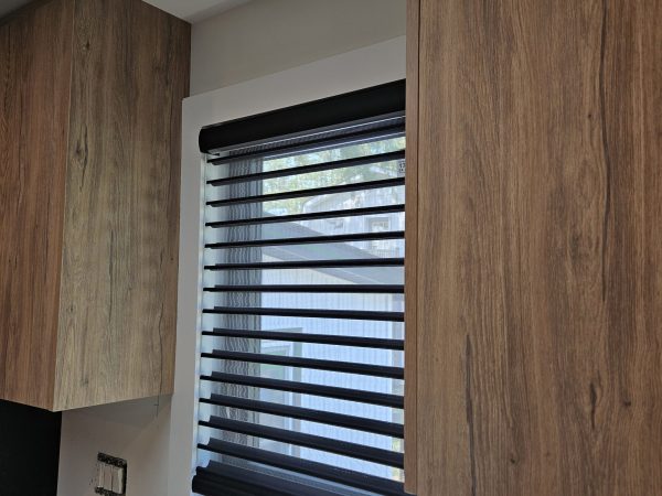 Zebra Blinds installed in a modern kitchen, featuring stylish black and white alternating stripes, framed by wooden cabinetry, enhancing light control and privacy.