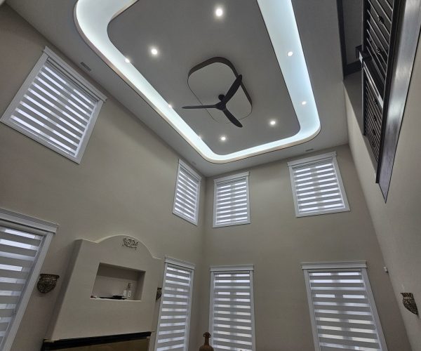 Interior view of a modern room featuring solar-powered motorized blinds on multiple windows, a sleek ceiling with recessed lighting, and a ceiling fan, showcasing an elegant and bright living space.